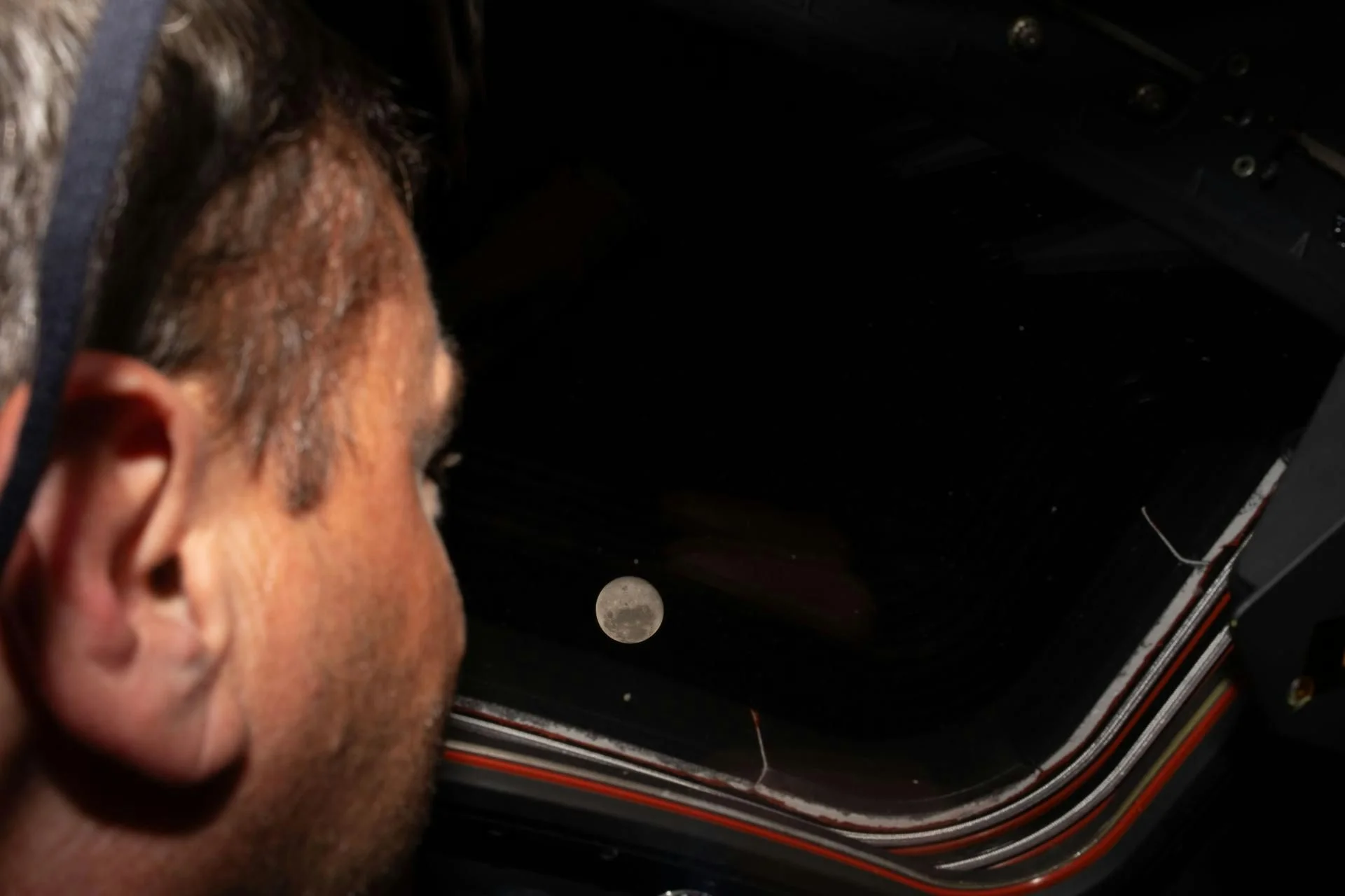 An astronaut looking out the window of the Orion spacecraft, where the full moon is visible in space.