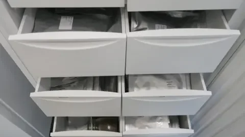 The National Botanical Garden of Wales A set of white laboratory drawers pulled open to reveal neatly stacked silver foil packets. Each packet contains stored seeds, labelled and organised for preservation.
