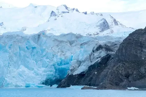 Getty Images A large glacier next to a large rock, with a river basin below