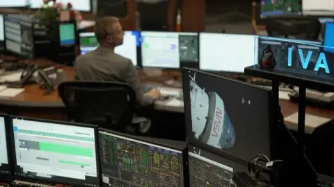 BBC/Kevin Church Mission control at the Johnson Space Center in Houston. Rows of computer screens with one worker sitting at their desk. 